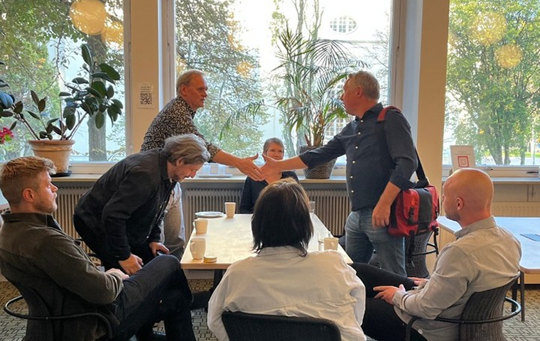 En grupp deltagare i ett samtalsrum möts i dialog och handslag. Bilden förmedlar personlig talarträning, kommunikationsutveckling och lärande genom möten, övning och reflektion.