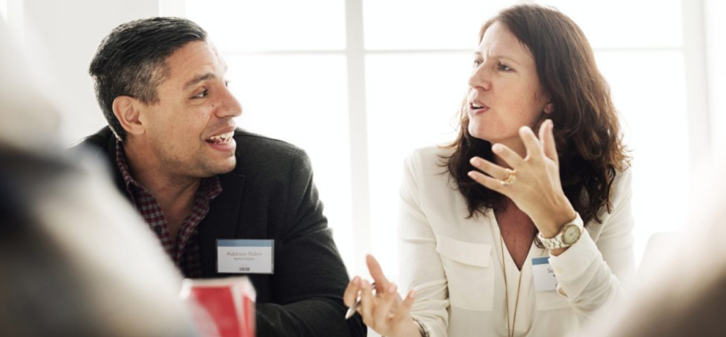 En kvinna sitter tillsammans med en man på en konferens och diskuterar livligt med inlevelse och levande kroppspråk, 

Bilden illustrerar betydelsen av inlevelse i kommunikation mellan två eller flera människor