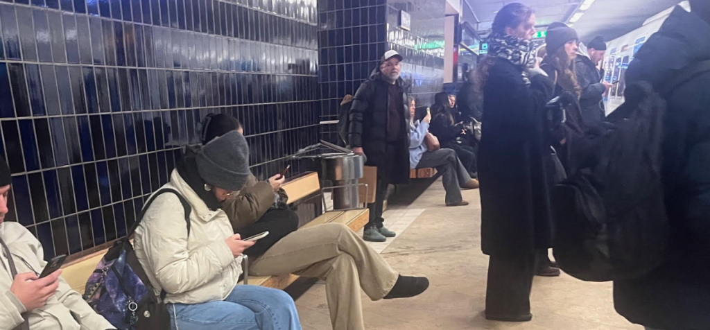 Hur skapar du trovärdig och pålitlig publikinteraktion i en tid av ständig uppkoppling? En grupp människor står tätt tillsammans i en stadsmiljö och rör sig genom ett offentligt rum. Flera personer tittar ner i sina mobiltelefoner med huvudet lätt böjt och axlarna något framåtdragna. De är klädda i vardagliga ytterkläder och rör sig parallellt utan ögonkontakt med varandra. Omgivningen är urban med ljus, rörelse och intryck som konkurrerar om uppmärksamheten, vilket förstärker känslan av konstant informationsflöde och splittrat fokus.