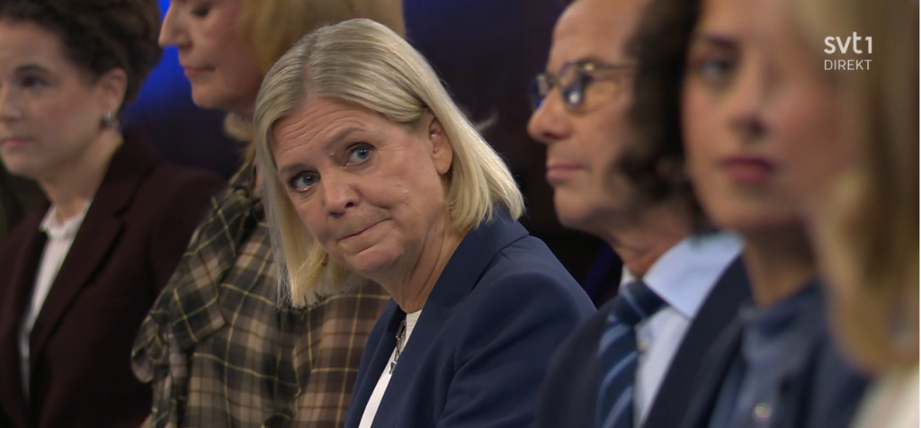 Hur påverkar kroppsspråk och ansiktsuttryck hur politiska budskap tas emot? Under en tv-sänd partiledardebatt sitter flera politiker bredvid varandra. I bildens centrum syns en blond kvinna i mörkblå kavaj som tittar åt sidan med lätt sammanpressade läppar och höjda ögonbryn. Runt henne sitter andra deltagare med varierande blickar och ansiktsuttryck. Bilden är från SVT1:s direktsändning.